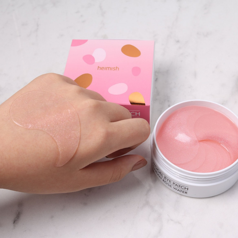Ręka trzymająca różowy Bulgarian Rose Hydrogel Eye Patch 60 sztuk od heimish i nakładająca maskę pod oczy.