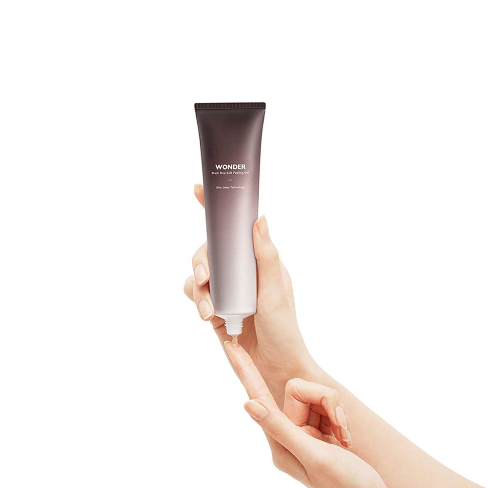 Ręka kobiety trzymającej tubę Haruhuru Wonders Black Rice Soft Peeling Gel 100 ml na białym tle.