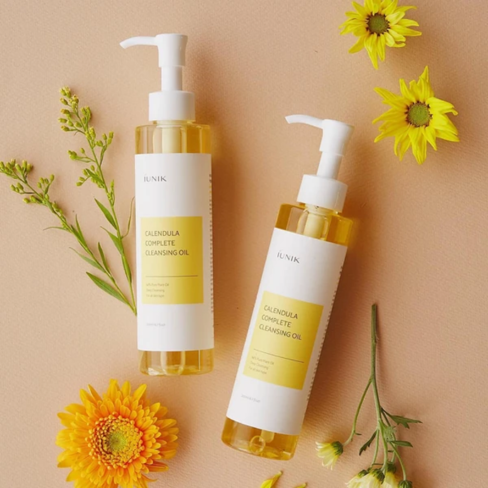 Dwie butelki iUNIK Calendula Complete Cleansing Oil 200ml z żółtymi kwiatami na beżowym tle, nasycone olejem roślinnym.
