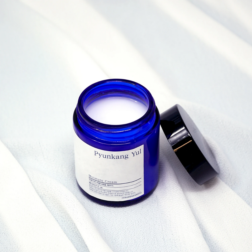 Niebieski słoik z pokrywką, która znajduje się na białej tkaninie, prezentujący nawilżające właściwości Pyunkang Yul's Moisture Cream 100ml.
