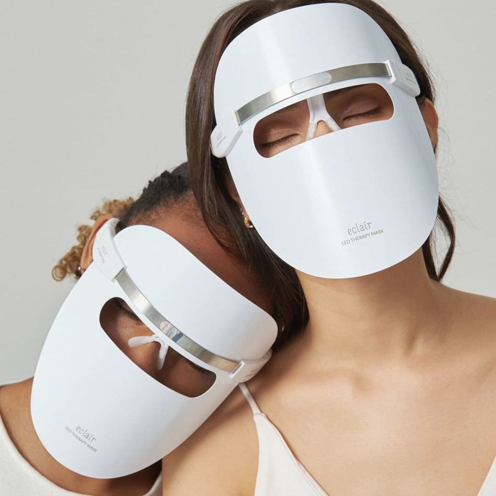 Dwie kobiety noszące białe maski demonstrują ECLAIR LED Therapy Mask dla poprawy kolorytu skóry.