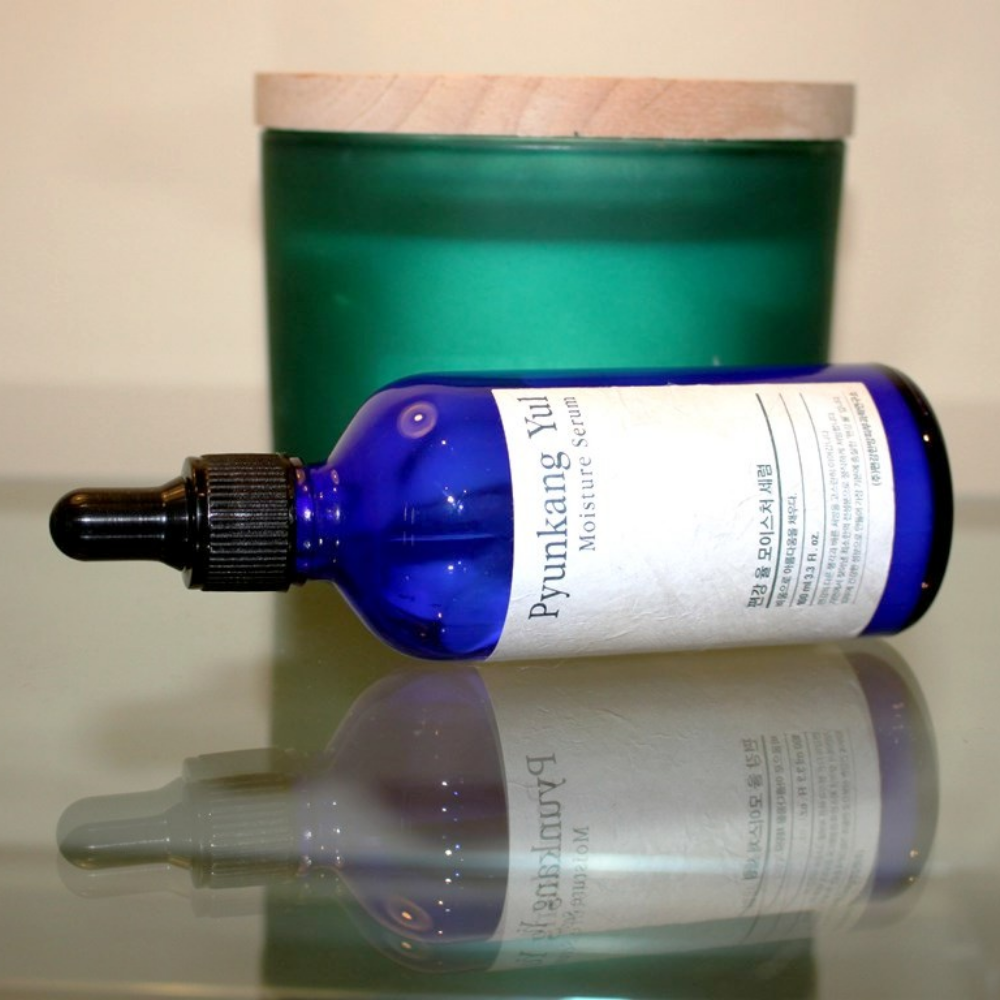 Butelka Pyunkang Yul Moisture Serum 100ml równoważy poziomy nawilżenia na stole obok świecy.