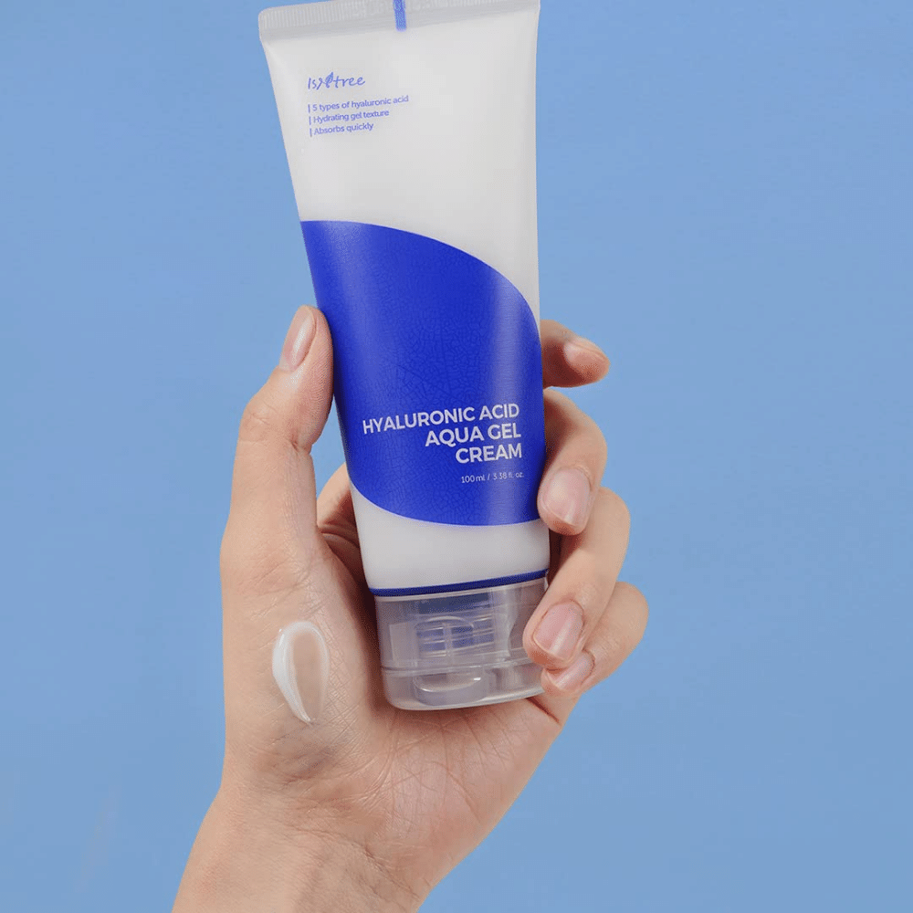 Ręka trzymająca tubę Isntree Hyaluronic Acid Aqua Gel Cream 100ml na niebieskim tle.