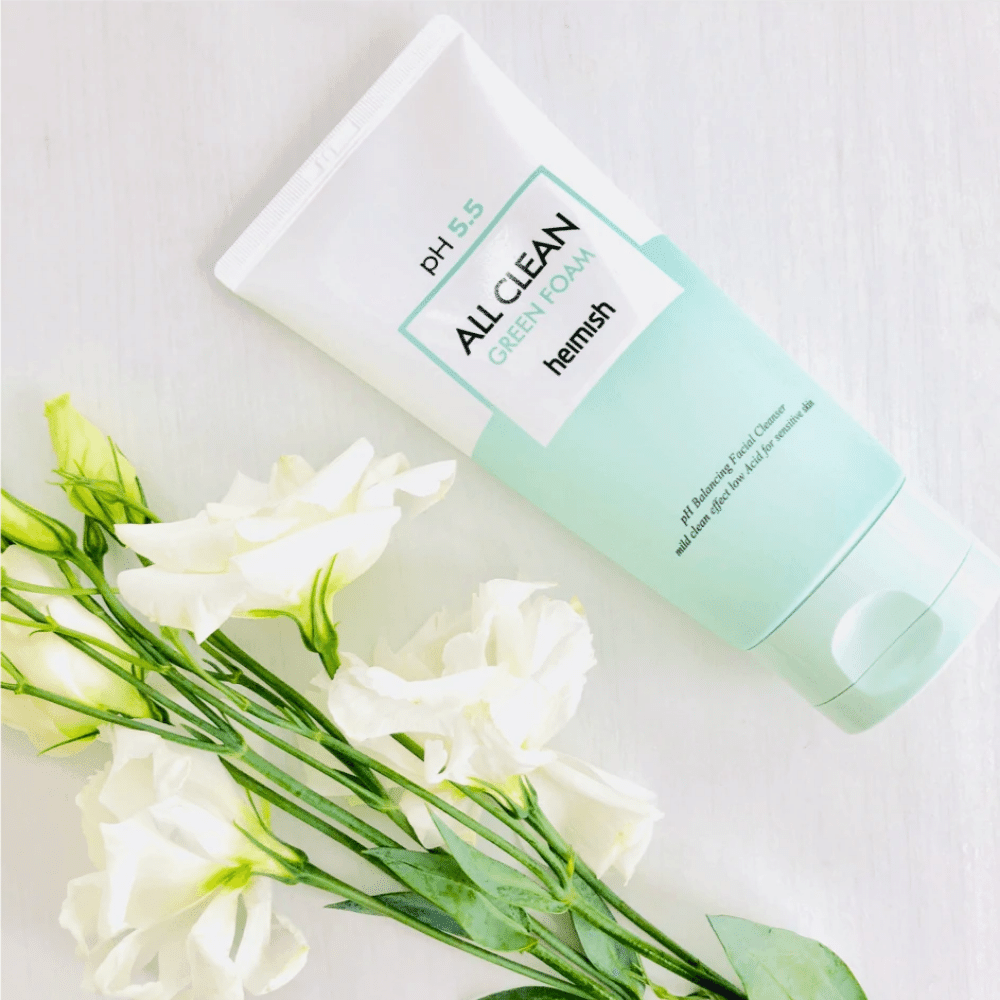 Tubka heimish All Clean Green Foam 150ml obok białych kwiatów.